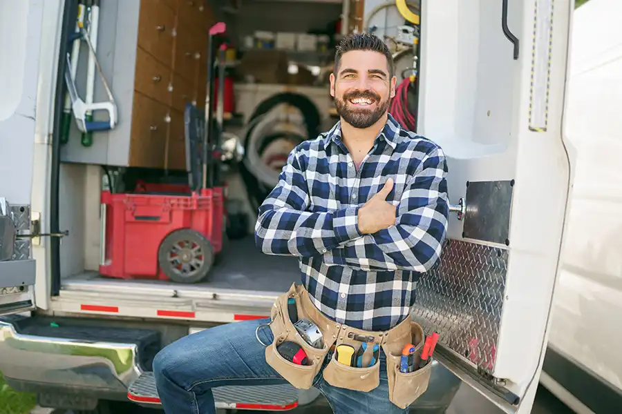 Ruby Electric, Inc.—A male electrician with a tool belt smiling in front of his van in Springfield, IL.